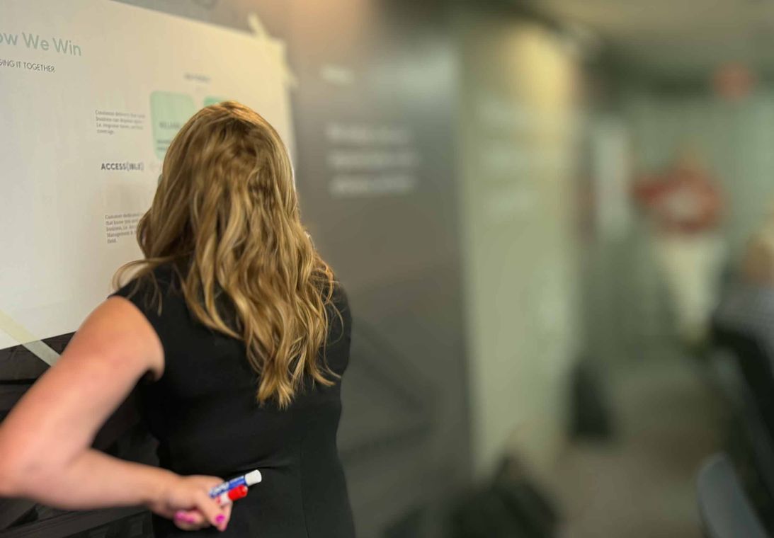 “How We Win” CX strategy workshop Facilitator leading a “How We Win” customer experience strategy workshop, writing on the board with a dry-erase marker