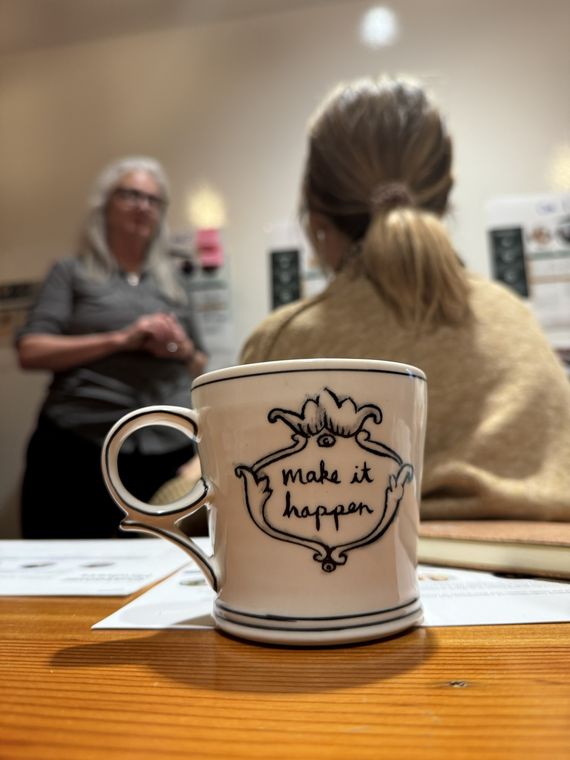 “Make it happen” CX workshop “Make it happen” mug on the table at a customer experience strategy workshop with participants in the background